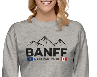 Puede incluir: Una sudadera gris con una silueta de montaña negra y el texto "Banff National Park" con una bandera canadiense y una bandera de provincia canadiense.