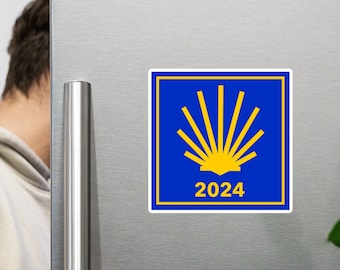 May include: A blue square sticker with a yellow scallop shell symbol and the text "2024" on a silver refrigerator.