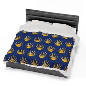 May include: A navy blue bedspread with a repeating pattern of gold seashells. The bedspread is on a bed with white sheets and pillows.
