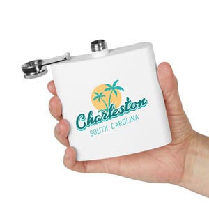 Könnte beinhalten: Weiße Edelstahl-Trinkflasche mit silbernem Verschluss und einer Grafik mit Palmen und einer gelben Sonne mit dem Text "Charleston, South Carolina".