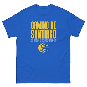 May include: A royal blue t-shirt with the text "Camino de Santiago" and "Buen Camino" in yellow. A yellow scallop shell symbol is below the text.