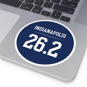 May include: A blue and white circle sticker with the text "Indianapolis 26.2" on a silver laptop.