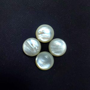 May include: Four round, white, iridescent pearls on a black background. The pearls have a smooth, reflective surface with subtle colour and texture variations, suggesting a natural origin. These pearls are likely used for jewellery making.