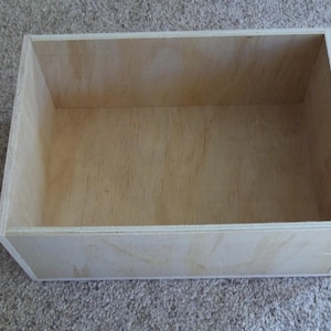 May include: A plain wooden box with a light brown finish. The box is empty and has a rectangular shape.