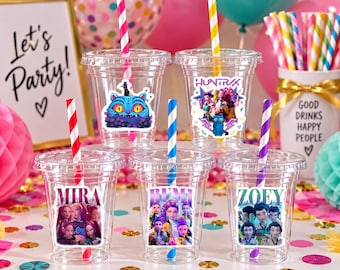 May include: Five clear plastic cups with lids and colourful striped straws. Each cup features a unique character sticker, including a blue cat and groups of people labelled Mira, Bumi, and Zoey. The cups are arranged on a surface with confetti.