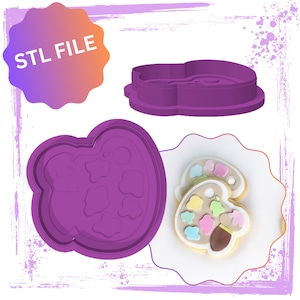 May include: Purple plastic cookie cutter shaped like a paint palette with a paintbrush. STL FILE is written on a pink and orange starburst shape.