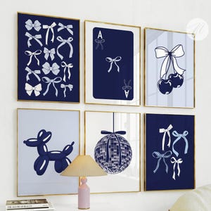 May include: Six framed art prints with gold frames. The prints feature various designs in shades of blue and white, including bows, playing card, cherries, a balloon dog, a disco ball, and more bows. The art is displayed on a white wall.