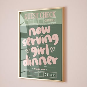 May include: A framed print with a gold border. The print features the words "GUEST CHECK" and "now serving girl dinner" in pink lettering on a green background. The print also includes the number "051893".