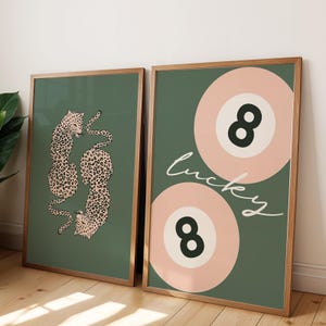May include: Two framed prints with a green background. The print on the left features a pair of leopards in a curled position. The print on the right features two pink and white 8-ball designs with the word "lucky" written in cursive.