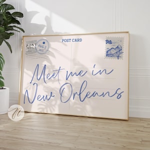 以下が含まれることがあります： 「Meet me in New Orleans」の文字が青い筆記体で書かれた、額入りのポストカードプリント。 ポストカードのデザインには、消印、切手、書き込み用の線が含まれています。 フレームは明るい金色です。