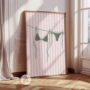 May include: A digital illustration of a green bikini hanging on a washing line against a pink and white striped background.