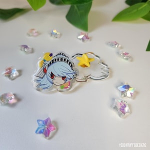 May include: A clear acrylic charm featuring a blue-haired anime character with red eyes, a yellow star, and a cloud-shaped charm. Scattered around are iridescent star-shaped embellishments. The charm is set against a white background with green leaves.