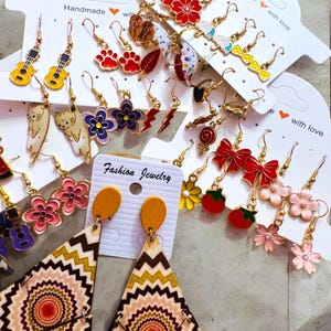 May include: Assortment of colorful dangle earrings with various designs, including flowers, musical notes, lightning bolts, and hearts. The earrings are displayed on white cards with the text "Handmade with love" and "Fashion Jewelry".