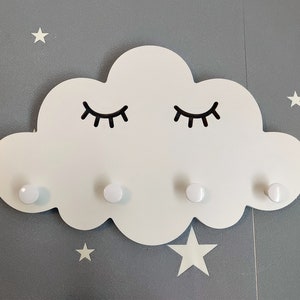 Op de afbeelding: Witte houten wolkvormige wandhaak met vier witte knoppen en zwarte wimpers.