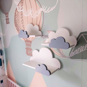 K&ouml;nnte beinhalten: Drei wei&szlig;e Wolkenf&ouml;rmige Regale mit grauen Wolkenakzenten, die an einer hellgr&uuml;nen Wand mit einem Hei&szlig;luftballonmuster montiert sind.