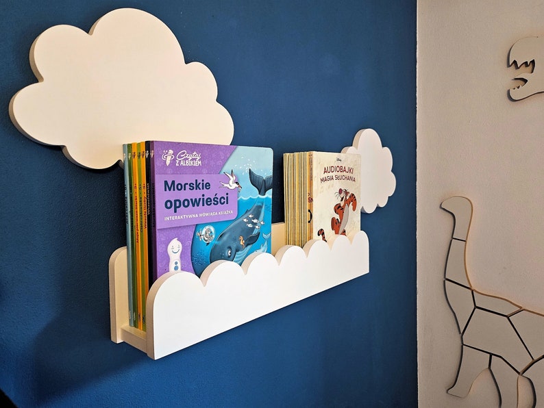 May include: White cloud-shaped bookshelf with two rows of books. The top row has a book titled "Audiobajki Magia Słuchania" and the bottom row has a book titled "Morskie Opowieści".