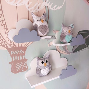 K&ouml;nnte beinhalten: Drei wei&szlig;e Regale in Wolkenform mit grauen Wolkenakzenten. Jedes Regal hat eine graue Pl&uuml;sch-Eule mit einem Herzmotiv auf der Brust. Die Eulen haben unterschiedlich farbige Herzen und Augen.