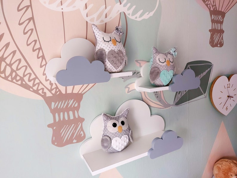 K&ouml;nnte beinhalten: Drei wei&szlig;e Regale in Wolkenform mit grauen Wolkenakzenten. Jedes Regal hat eine graue Pl&uuml;sch-Eule mit einem Herzmotiv auf der Brust. Die Eulen haben unterschiedlich farbige Herzen und Augen.