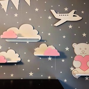 Op de afbeelding: Vier witte houten wolkvormige planken met roze wolkenaccenten, en een witte houten berenplank met een roze hart, allemaal tegen een grijze achtergrond met witte sterren.