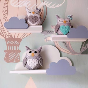 K&ouml;nnte beinhalten: Drei wei&szlig;e wolkenf&ouml;rmige Regale mit grauen Wolken und grauen Eulenfiguren. Die Eulen haben ein Herzdesign auf der Brust und sitzen auf den Regalen.