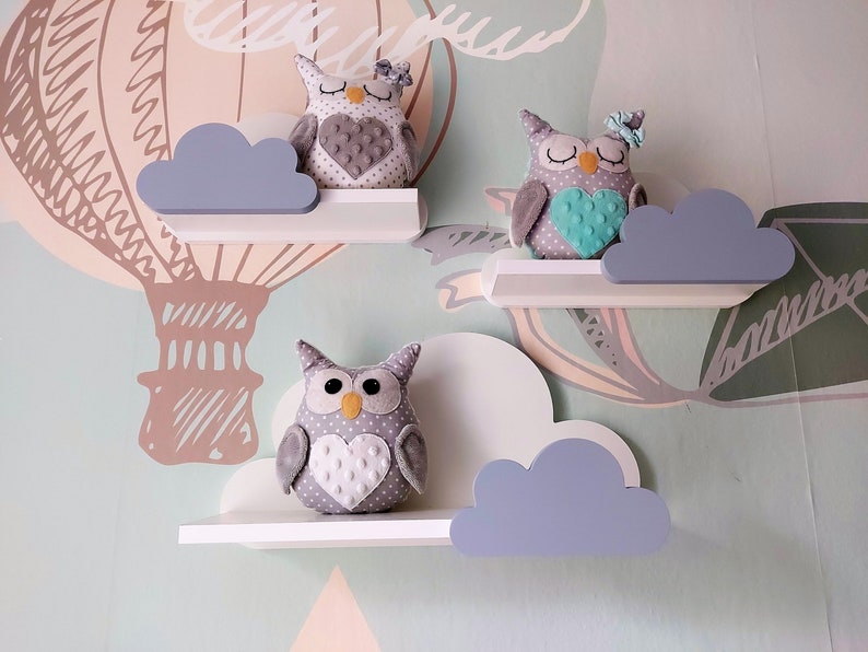 K&ouml;nnte beinhalten: Drei wei&szlig;e wolkenf&ouml;rmige Regale mit grauen Wolken und grauen Eulenfiguren. Die Eulen haben ein Herzdesign auf der Brust und sitzen auf den Regalen.