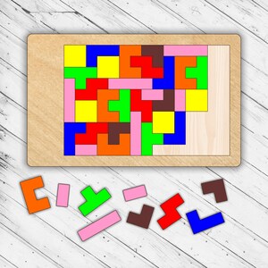 Może przedstawiać: Drewniana plansza do układania puzzli z różnymi kolorowymi klockami. Klocki są ułożone w wzór, a wokół planszy rozrzucone są dodatkowe klocki. Klocki są w kolorze czerwonym, niebieskim, zielonym, żółtym, pomarańczowym, różowym i brązowym.