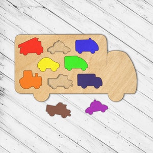May include: Wooden toy truck with a variety of colorful vehicle shapes that fit into the truck bed. The shapes include a fire truck, a police car, a taxi, a pickup truck, a tractor, and a van.
