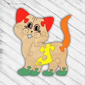 May include: A wooden puzzle of a cat with red ears, a yellow belly, and green shoes. The cat is smiling and has big eyes.