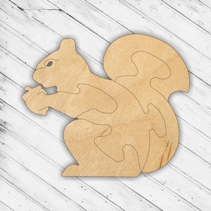 May include: A wooden cutout of a squirrel holding a nut in its paws. The squirrel is in a sitting position with its tail curled behind it.