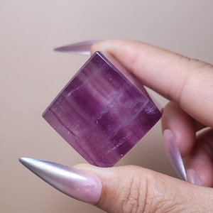 May include: A purple fluorite cube crystal with striations and a smooth, polished surface.