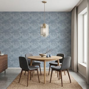 Puede incluir: Un comedor con una mesa redonda de madera y cuatro sillas grises tapizadas sobre una alfombra tejida. La pared está cubierta con papel tapiz azul y blanco con un patrón de olas, iluminado por una lámpara colgante geométrica.
