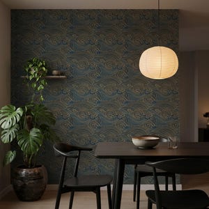 May include: Wallpaper featuring a repeating pattern of stylized dark blue and gold waves. The design covers the wall behind a dark wooden dining table with black chairs, a potted monstera plant, a small wall shelf, and a round paper pendant light.