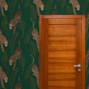 Puede incluir: Un papel tapiz verde con un patrón repetitivo de hojas de plátano de hoja de oro y animales de estampado de leopardo. Una puerta de madera está en el lado derecho de la imagen.