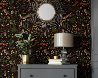 May include: A dark wallpaper featuring a repeating pattern of brown hares, squirrels, owls, snakes, snails, moths, mushrooms, ferns, and golden crescent moons and stars. A sunburst mirror, a table lamp, and books sit on a gray dresser.