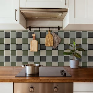 May include: A modern kitchen scene featuring a stainless steel pot on a black stovetop. The backsplash has a checkered pattern in shades of green, gray, and black. Wooden cutting boards and a pot holder hang above the stove. A potted plant sits on the countertop.