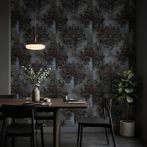 Puede incluir: Un comedor con una mesa de madera oscura, sillas negras, un jarrón con follaje verde y una lámpara colgante. La pared está cubierta con papel tapiz oscuro con un patrón de damasco negro y rojo intenso sobre un fondo gris texturizado.