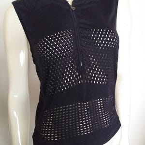 Puede incluir: Una camiseta negra sin mangas de malla con cierre de cremallera. La malla tiene un patrón geométrico.