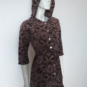 May include: A brown hooded dress with a paisley pattern and button fastening. The dress has a cinched waist and a flowing skirt.