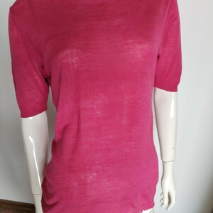 May include: A short-sleeved, magenta-colored mock turtleneck shirt. The shirt has a slightly sheer appearance and a ribbed neckline and hem. The garment is displayed on a mannequin.