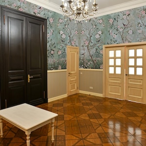 May include: A room with light wood floors and a floral wallpaper. There are two sets of double doors, one set is dark wood and the other is light wood. A small white table sits in the center of the room.