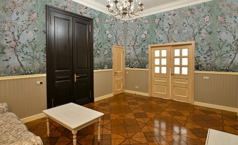 May include: A room with light wood floors and a floral wallpaper. There are two sets of double doors, one set is dark wood and the other is light wood. A small white table sits in the center of the room.