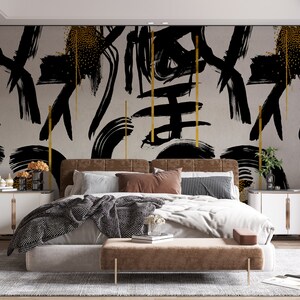 May include: A bedroom with a bed featuring a black and gold abstract brushstroke patterned headboard and a brown upholstered bed frame. The bed is dressed in white bedding with a black and white patterned throw blanket. There are two nightstands with gold accents on either side of the bed.