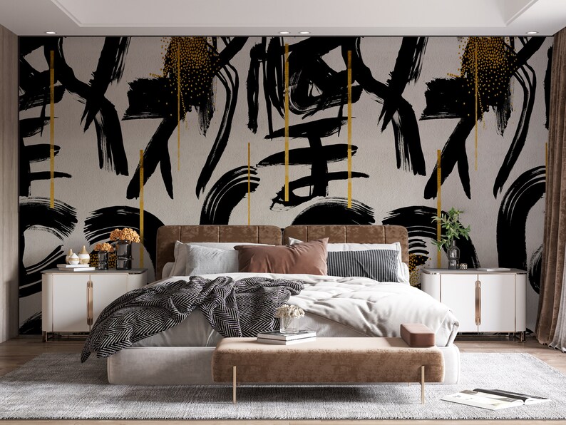 May include: A bedroom with a bed featuring a black and gold abstract brushstroke patterned headboard and a brown upholstered bed frame. The bed is dressed in white bedding with a black and white patterned throw blanket. There are two nightstands with gold accents on either side of the bed.