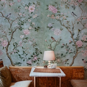 May include: A light green wallpaper with a floral pattern featuring pink flowers and small birds. A wooden table with a white tabletop and a lamp sits in front of the wallpaper.
