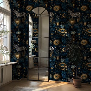 Op de afbeelding: Donkerblauw behang met een herhalend patroon van zebra's, ogen, manen en zonnen in goud en blauw. Het behang bevindt zich in een kamer met een grote boogspiegel en een raam. Een potplant staat in de hoek.