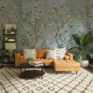 May include: A tan leather sectional sofa with a chaise lounge, two throw pillows, and a black coffee table with a lower shelf. The sofa is in front of a wall with a floral wallpaper featuring pink flowers and birds.