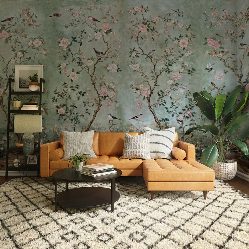 May include: A tan leather sectional sofa with a chaise lounge, two throw pillows, and a black coffee table with a lower shelf. The sofa is in front of a wall with a floral wallpaper featuring pink flowers and birds.