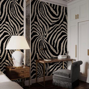 May include: A bedroom with zebra print wallpaper, a wooden desk with a gold frame, and a gray upholstered chair. A white lamp sits on a wooden nightstand. The room has white cabinets and a dark wood floor.