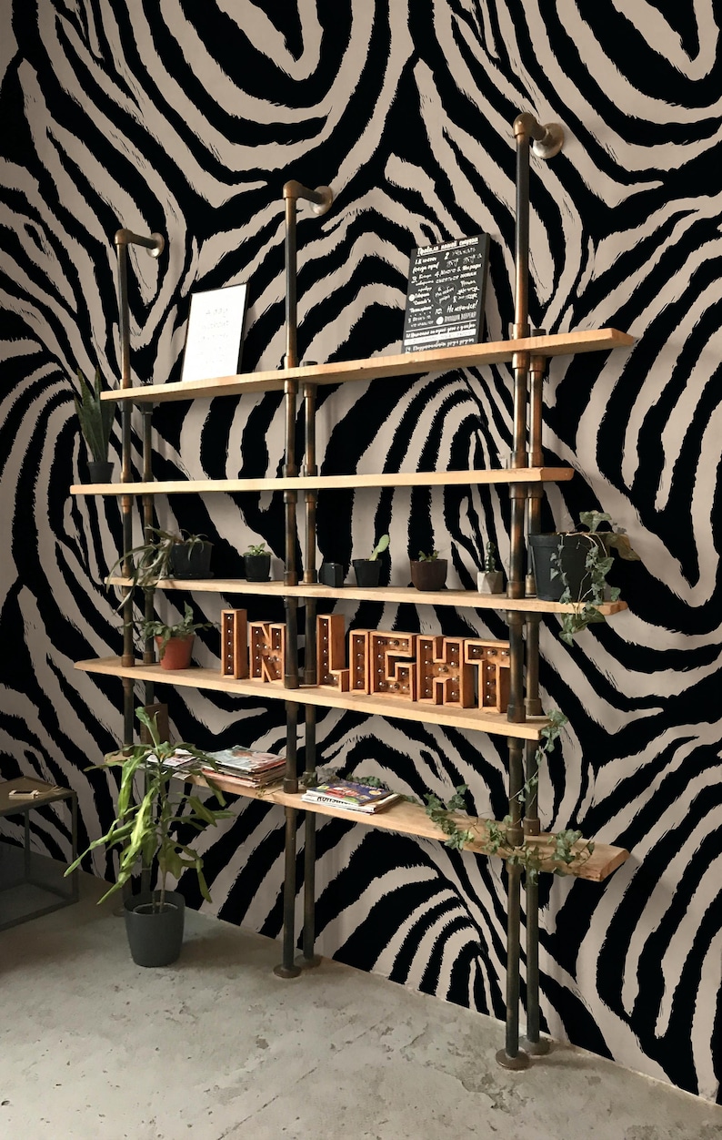 May include: A multi-tiered wooden shelf unit with metal piping supports, displaying potted plants, magazines, and a lighted sign that reads "IN LIGHT." The backdrop is a black and white zebra stripe pattern.