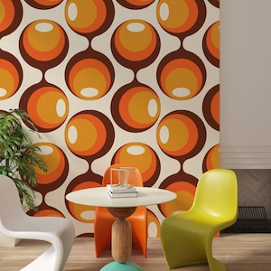 May include: A retro-style interior featuring a wallpaper with a repeating pattern of brown, orange, and yellow circles. The room includes a white table, a white chair, an orange chair, and a yellow chair. A potted plant is visible on the left.